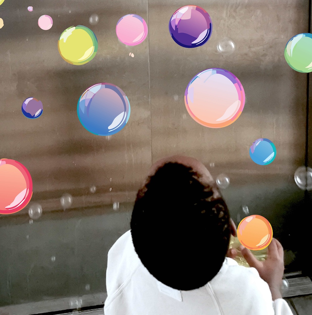 child from behind looking at colorful soap bubbles